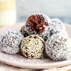 Leckeres energy balls rezept: Schokoladige Kugeln mit Kokosraspeln und Sesam auf einem Teller.