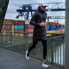 Mann joggt bei Regen über eine Brücke im Hafen. Container und Kräne im Hintergrund.