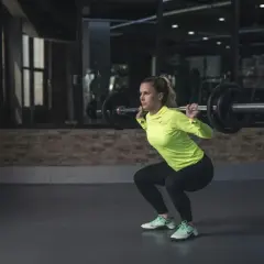 Frau macht Kniebeugen mit Langhantel. Sie ist fokussiert und stark, bereit für ihr Training. Kiffen und Sport – eine Kombination, die sie inspiriert.