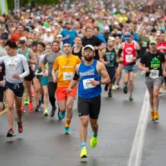 Läufer beim Halbmarathon Europa. Viele Teilnehmer in bunten Trikots, einige mit Startnummern, kämpfen sich über die nasse Straße.