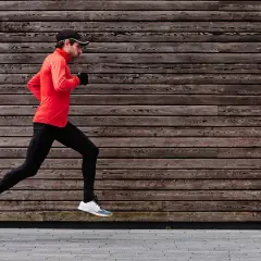 Ein Mann im roten Shirt und schwarzer Hose macht einen kraftvollen **crescendo lauf** vor einer Holzwand.