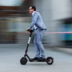 Mann im Anzug fährt mit einem E-Scooter durch Belgien.