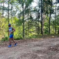 Läufer mit Startnummer 18 beim Plankenfelser Waldlauf, umgeben von hohen Bäumen und Sonnenschein.
