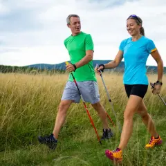 Ein Paar genießt das Power Walking auf einem Feldweg, umgeben von hohem Gras und sanften Hügeln.