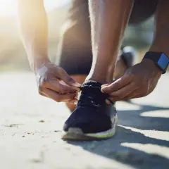 Hände binden die Schnürsenkel von Laufschuhen. Die Sonne scheint warm auf den Sand.