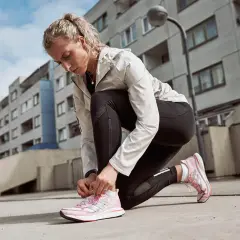 Läuferin kniet am Boden und bindet ihre neuen, pinken Laufschuhe ein. Perfekt zum Einlaufen!
