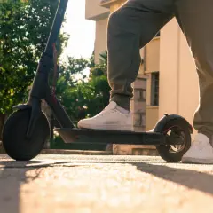 Person steht auf einem e scooter ohne kennzeichen, bereit für die Fahrt im warmen Sonnenlicht.