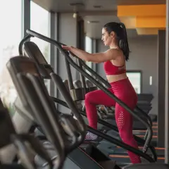 Frau im Fitnessstudio macht ein Stairmaster Workout. Sie trägt ein rotes Sport-Outfit und trainiert intensiv.
