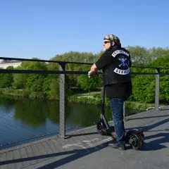 Mann auf E-Scooter mit "TRITTBRETT GERMANY" Aufnäher auf Weste. Er erklärt, wie funktioniert ein E-Scooter, während er auf einer Brücke steht.