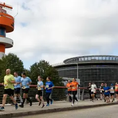 Läufer bei der Airport Race Hamburg, vorbei an einem markanten orange-weißen Turm und einem modernen Gebäude.