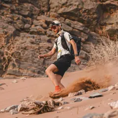 Läufer im Marathon des Sables wirbelt Sand auf. Die extreme Wüstenlandschaft fordert alles.