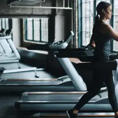 Frau im Fitnessstudio beim Laufband Training, mit Kopfhörern und Wasserflasche.