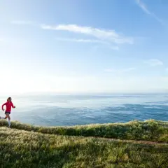 Läuferin auf Küstenpfad, trainiert für Marathon unter 4 Stunden. Weite See und Himmel.