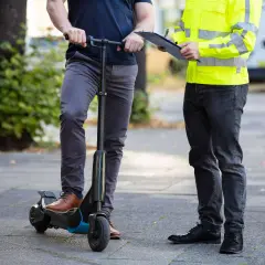 Mann auf e-scooter in Spanien, während ein anderer Mann mit Warnweste Notizen macht.