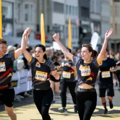 Läufer feiern Zieleinlauf beim Marathon. Ein Mann und zwei Frauen mit Startnummern, die Teil des Marathon Kalenders sind, jubeln.