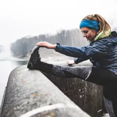 Zwei Frauen dehnen sich vor dem Laufen im Winter an einem Flussufer.