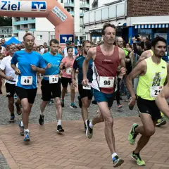 Läufer beim Europalauf Neustadt, einige mit Startnummern wie 49, 96 und 21. Sie rennen unter einem Zielbogen hindurch.