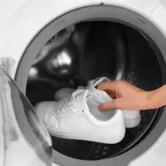 Weiße Laufschuhe werden in eine Waschmaschine gelegt.