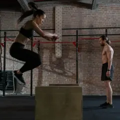 Frau springt auf eine Box, um Kondition aufzubauen. Mann beobachtet sie im Fitnessstudio.