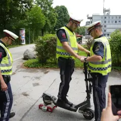 Polizisten prüfen einen E-Scooter. Einer steht drauf, der andere hält ihn fest. Ein Messgerät ist am Hinterrad angebracht.