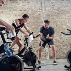 Männer trainieren intensiv beim Spinning. Ein Trainer motiviert die Sportler, die auf ihren Rädern strampeln.