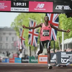Läufer Sawe überquert die Ziellinie, vielleicht ein neuer weltrekord 5km. Britische Flaggen wehen im Hintergrund.