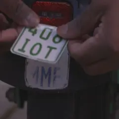 Hände befestigen ein neues e-scooter nummernschild mit der Aufschrift "408 10T" über einem alten, abgenutzten Kennzeichen.