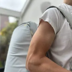 Mann mit Rucksack, der beim Anziehen der Jacke **Schmerzen im Oberarm** spürt.