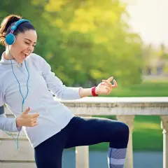 Frau mit Kopfhörern tanzt und singt beim Laufen im Park. Die Musik zum Laufen gibt ihr Energie.