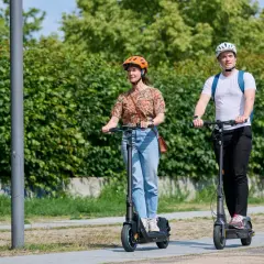 Mann und Frau fahren E-Scooter nebeneinander. Der Unterschied E-Roller und E-Scooter ist hier nicht ersichtlich, beide sind auf dem Weg.