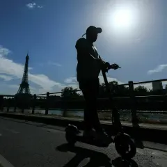 Mann fährt mit einem E-Scooter in Frankreich, die Silhouette des Eiffelturms im Hintergrund.