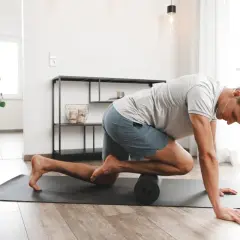 Mann behandelt sein Schienbeinkantensyndrom selbst mit einer Faszienrolle auf einer Matte.