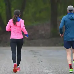Zwei Läufer, eine Frau in Pink und ein Mann in Blau, genießen die frische Luft. Sie zeigen, was bringt joggen: Fitness und Wohlbefinden.