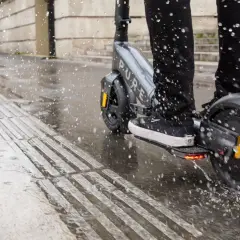 Ein e-scooter bei regen spritzt durch Pfützen auf dem nassen Gehweg.
