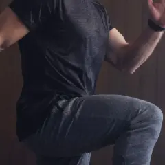 Mann in Sportkleidung, der auf der Stelle läuft, mit erhobenem Knie und ausgestrecktem Arm.