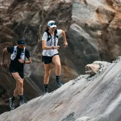 Zwei Läufer meistern einen steilen, felsigen Hang. Sie sind Teil eines Ultramarathons, einer extremen Laufdisziplin.