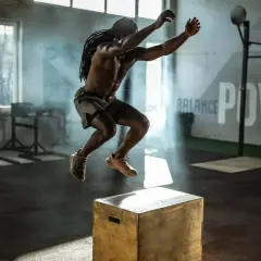 Mann macht explosive Box Jumps in einem Fitnessstudio. Rauch und Lichteffekte unterstreichen die Dynamik.