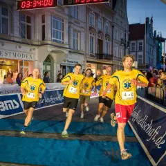 Läufer im Ziel beim hella marathon rostock. Gelbe Trikots mit "Ambulanz Millich" und Startnummern.