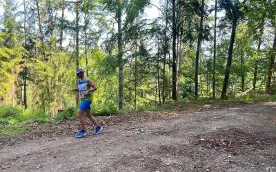 Läufer mit Startnummer 18 beim Plankenfelser Waldlauf, umgeben von hohen Bäumen und Sonnenschein.