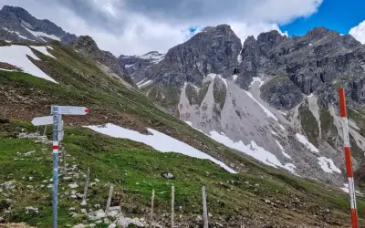 Wanderwegweiser am Widderstein Trail. Grüne Hänge mit Schneefeldern und steile Felsgipfel im Hintergrund.