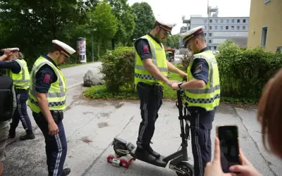 Polizisten prüfen einen E-Scooter. Einer steht drauf, der andere hält ihn fest. Ein Messgerät ist am Hinterrad angebracht.