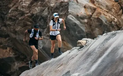 Zwei Läufer meistern einen steilen, felsigen Hang. Sie sind Teil eines Ultramarathons, einer extremen Laufdisziplin.