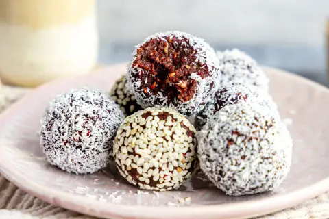 Leckeres energy balls rezept: Schokoladige Kugeln mit Kokosraspeln und Sesam auf einem Teller.