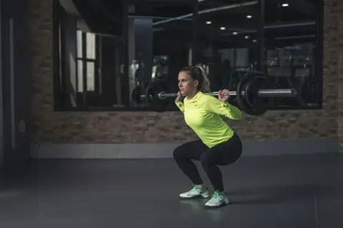 Frau macht Kniebeugen mit Langhantel. Sie ist fokussiert und stark, bereit für ihr Training. Kiffen und Sport – eine Kombination, die sie inspiriert.