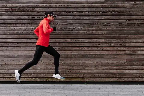 Ein Mann im roten Shirt und schwarzer Hose macht einen kraftvollen **crescendo lauf** vor einer Holzwand.