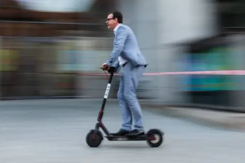 Mann im Anzug fährt mit einem E-Scooter durch Belgien.