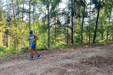 Läufer mit Startnummer 18 beim Plankenfelser Waldlauf, umgeben von hohen Bäumen und Sonnenschein.