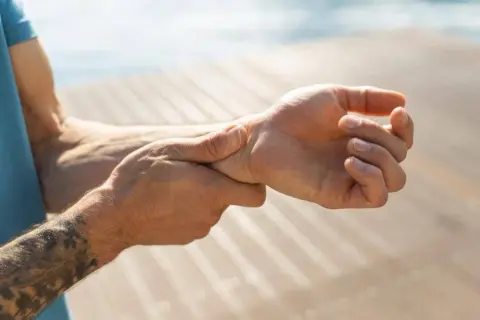 Mann hält sich das Handgelenk, da er Schmerzen im Handgelenk hat.