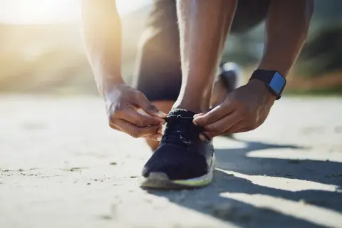 Hände binden die Schnürsenkel von Laufschuhen. Die Sonne scheint warm auf den Sand.