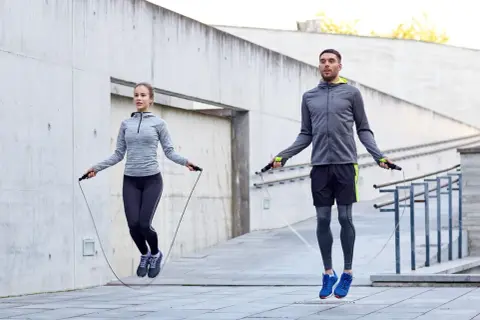 Ein Mann und eine Frau springen Seil. Sie trainieren draußen und zeigen, wie effektiv ist seilspringen für die Fitness.